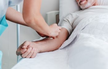 Caucasian nurse putting dropper to ill male patient in hospital bed. Healthcare and treatments concept. Senior man recovering after Covid 19
